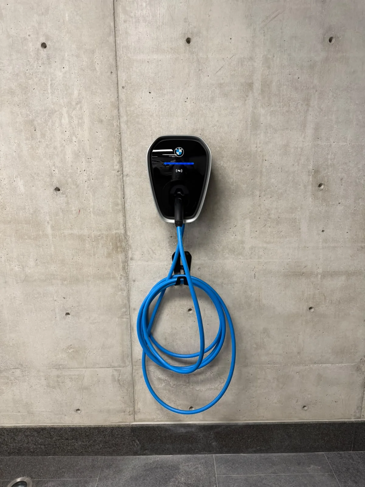 Cargador para vehículo eléctrico montado en concreto, con cable azul en su soporte.