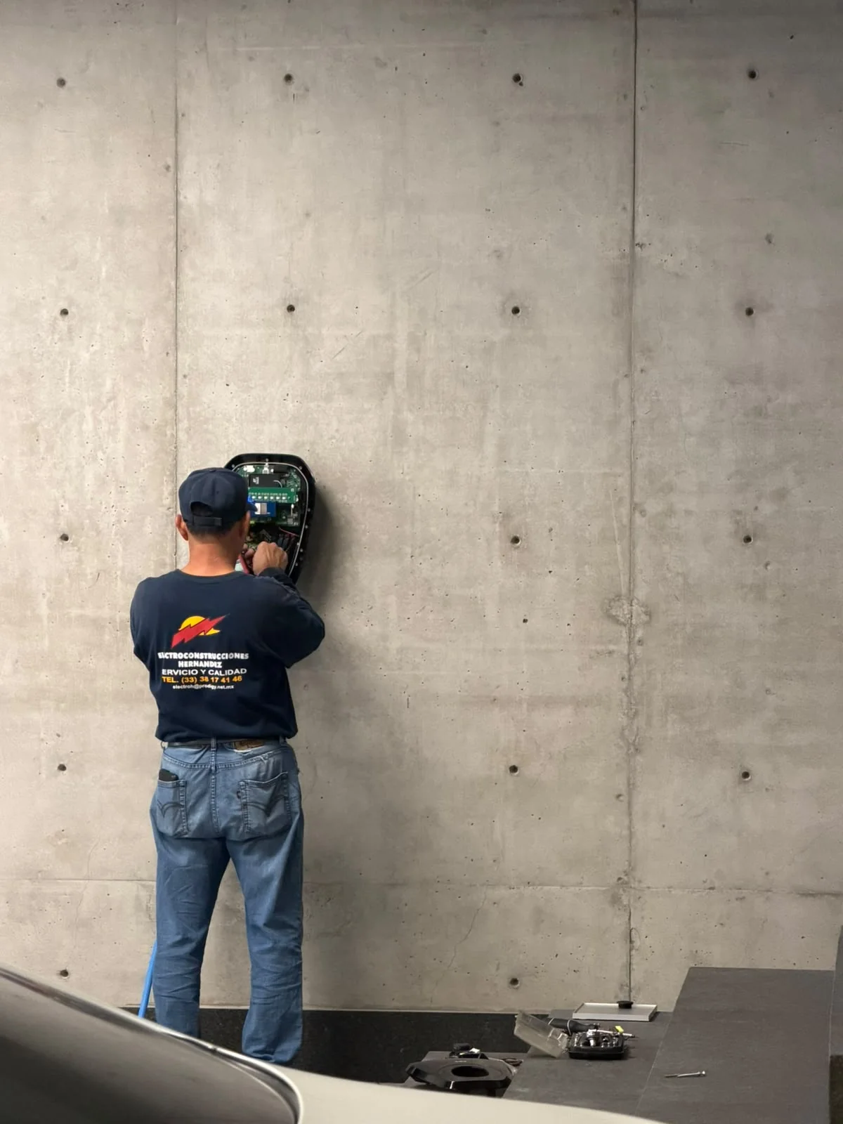 Técnico de ElectroH trabajando en la conexión de un equipo fijado a un muro de concreto.