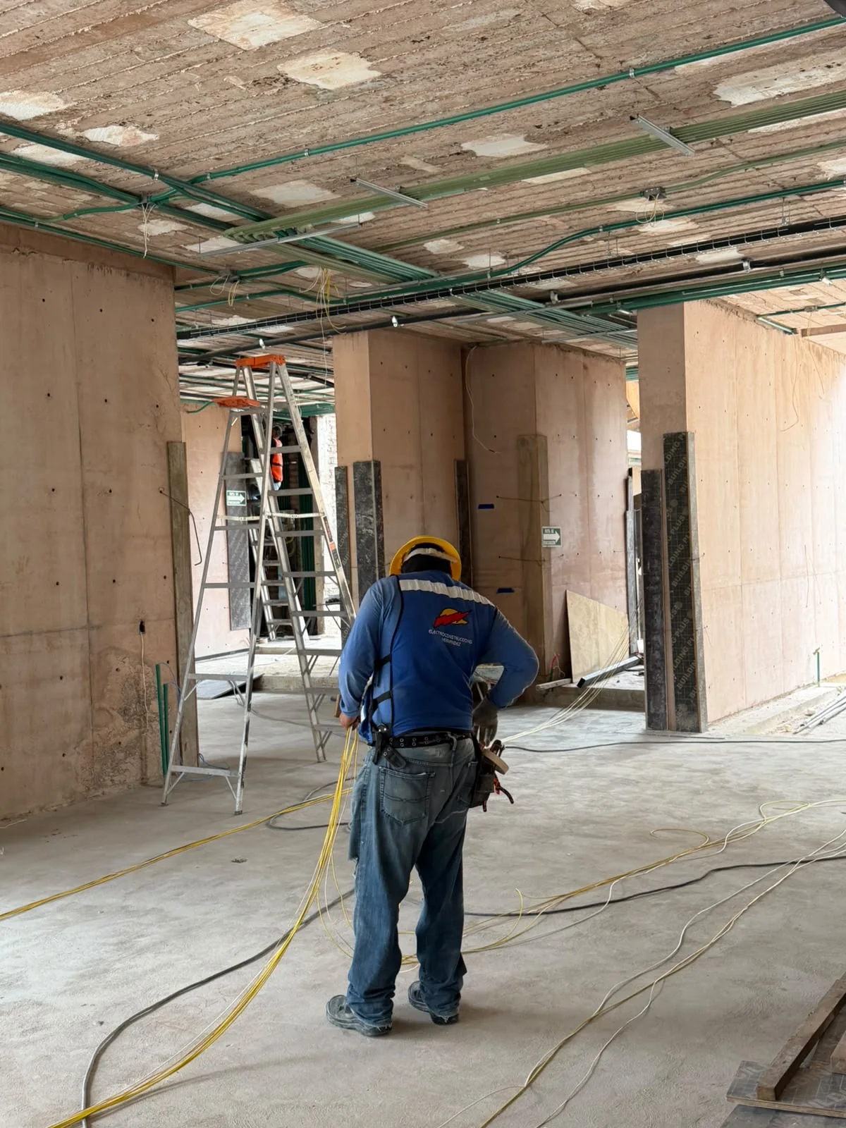 Técnico de ElectroH con casco amarillo y herramientas, trabajando con conductores en un interior en construcción.